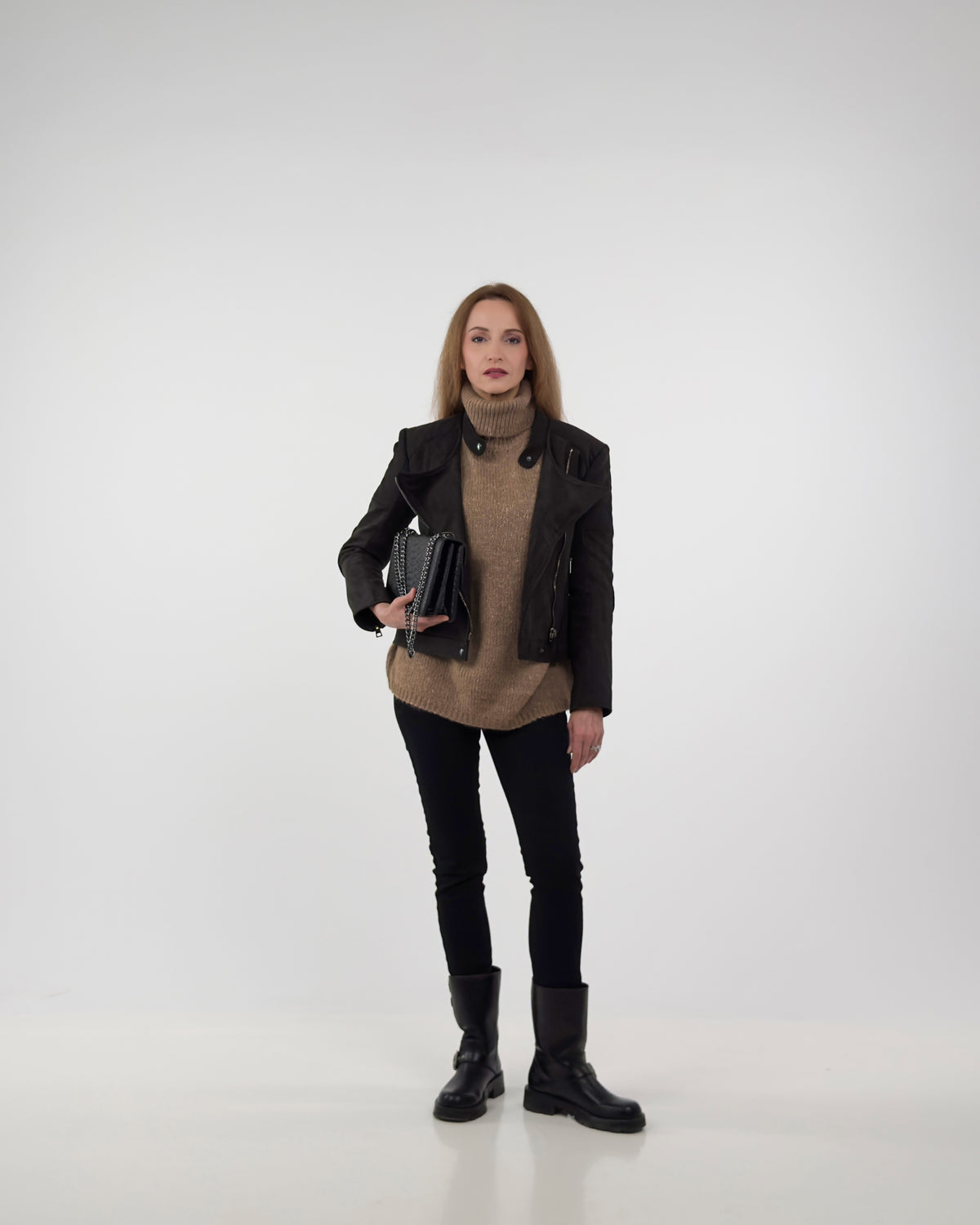 Full-length styling of the Diva biker jacket in black technical suede, layered over a tan knit sweater with black trousers and boots