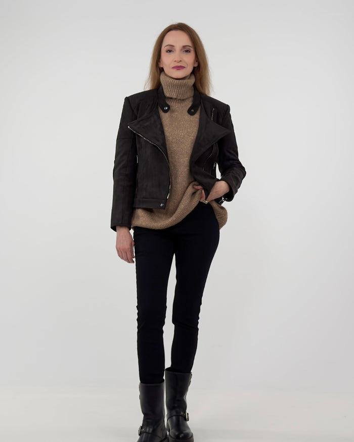 The Diva biker jacket in black technical suede, styled with an oversized tan turtleneck and black trousers for a sophisticated, comfortable look.